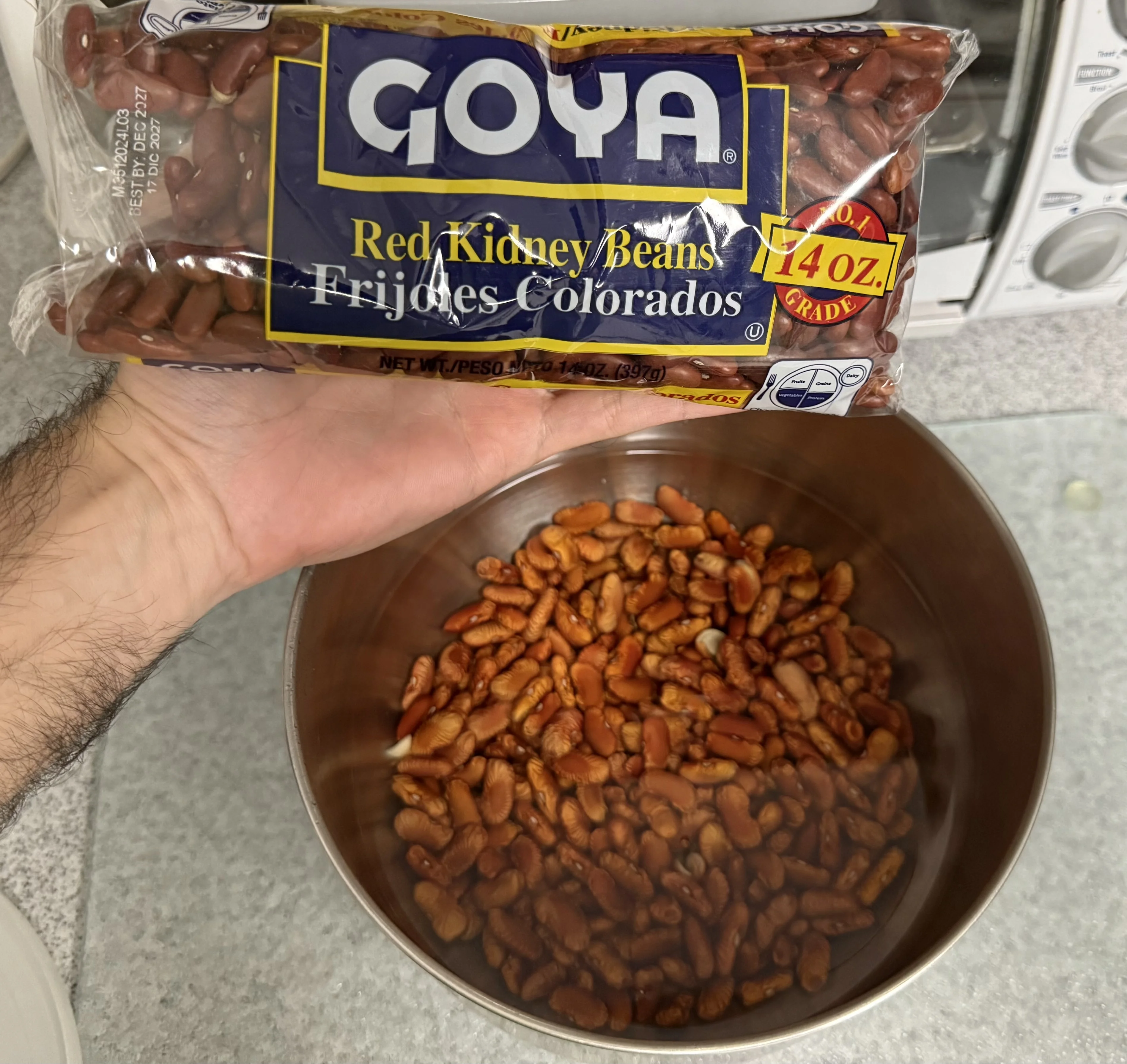 A bag of Goya red kidney beans held above a bowl of soaked beans