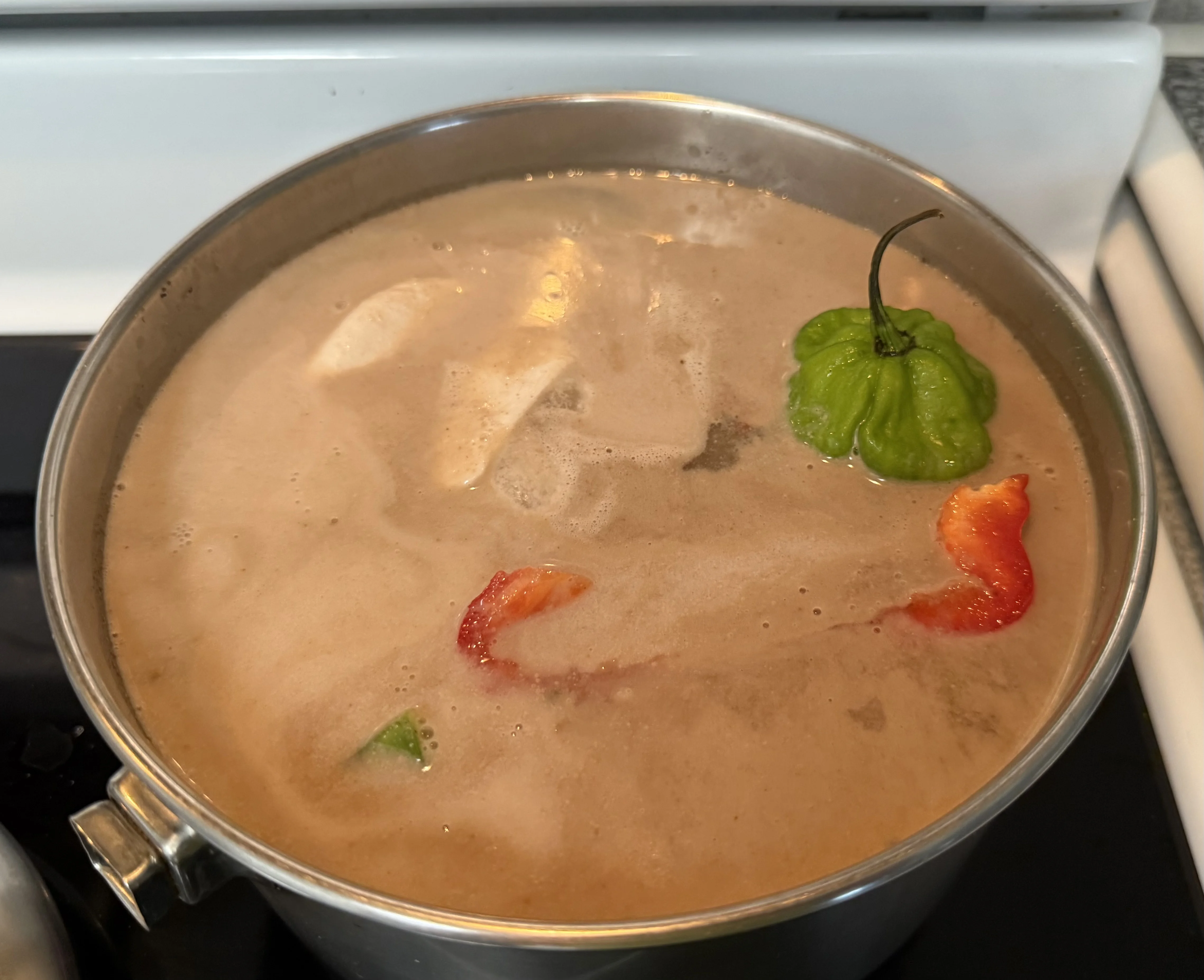A pot of beans with coconut milk melting in, a whole green scotch bonnet and pieces of red pepper