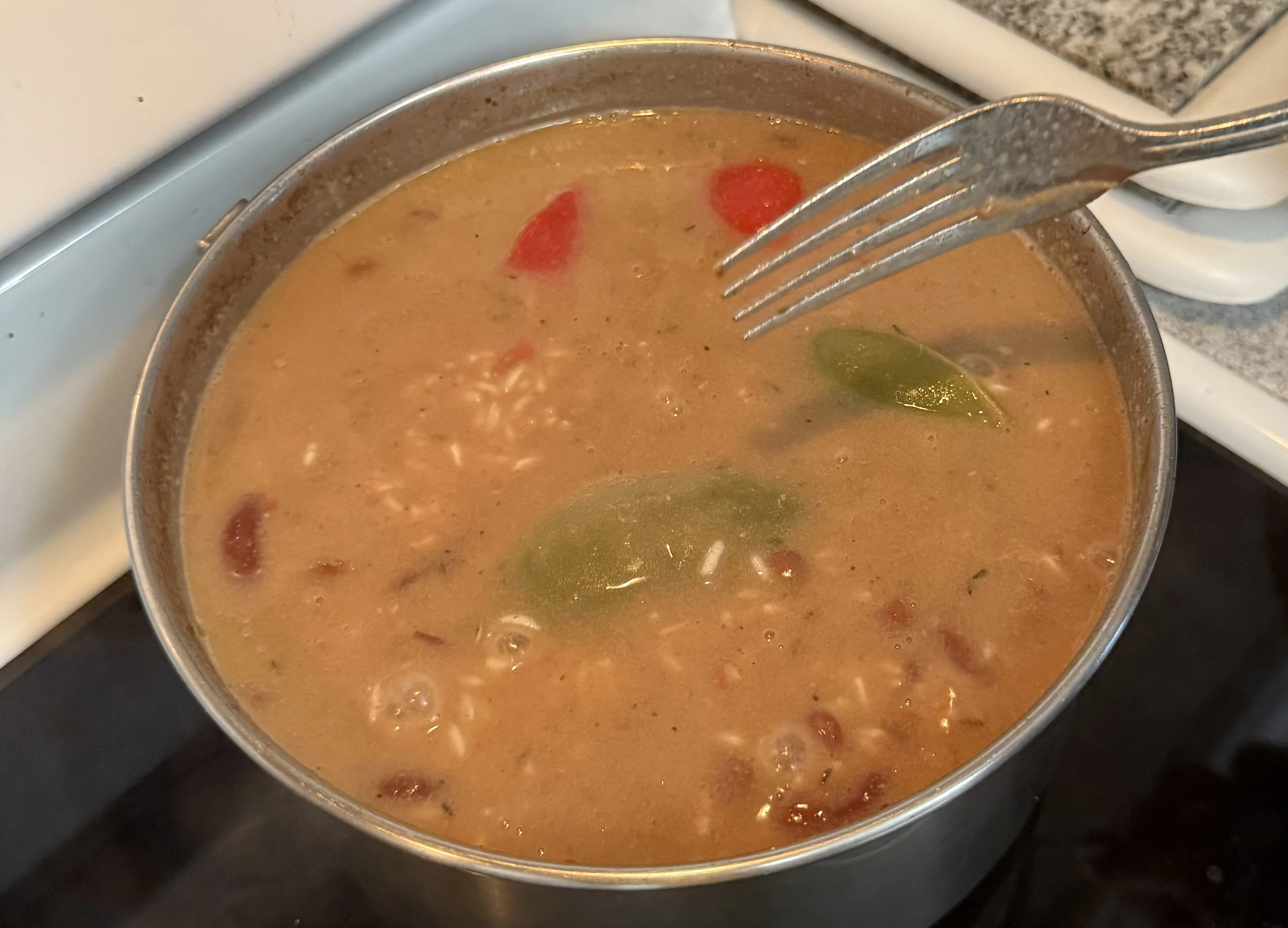 A fork testing the liquid in a pot of rice and beans with green and red pepper pieces
