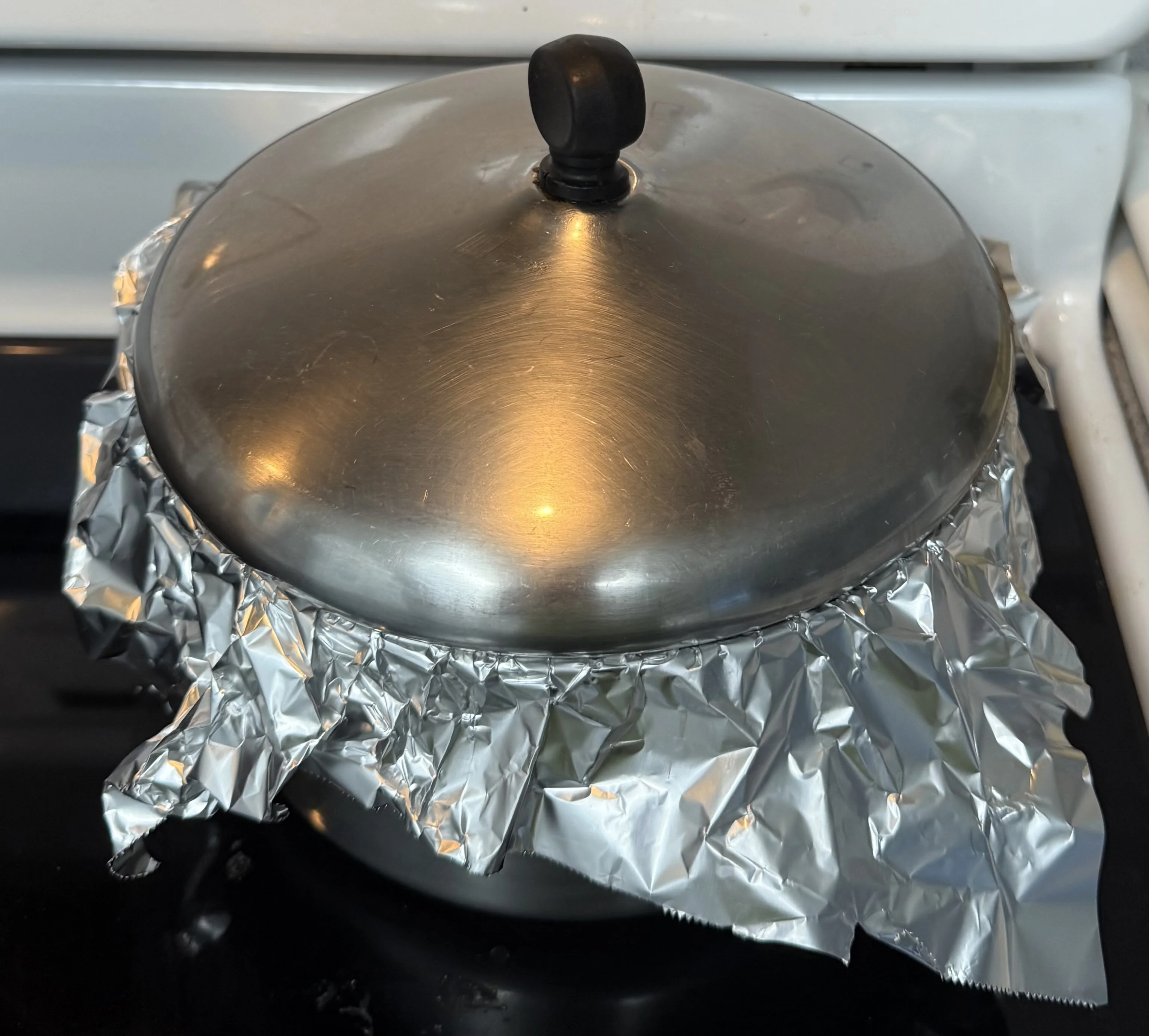 A pot covered tightly with foil and a lid on the stove