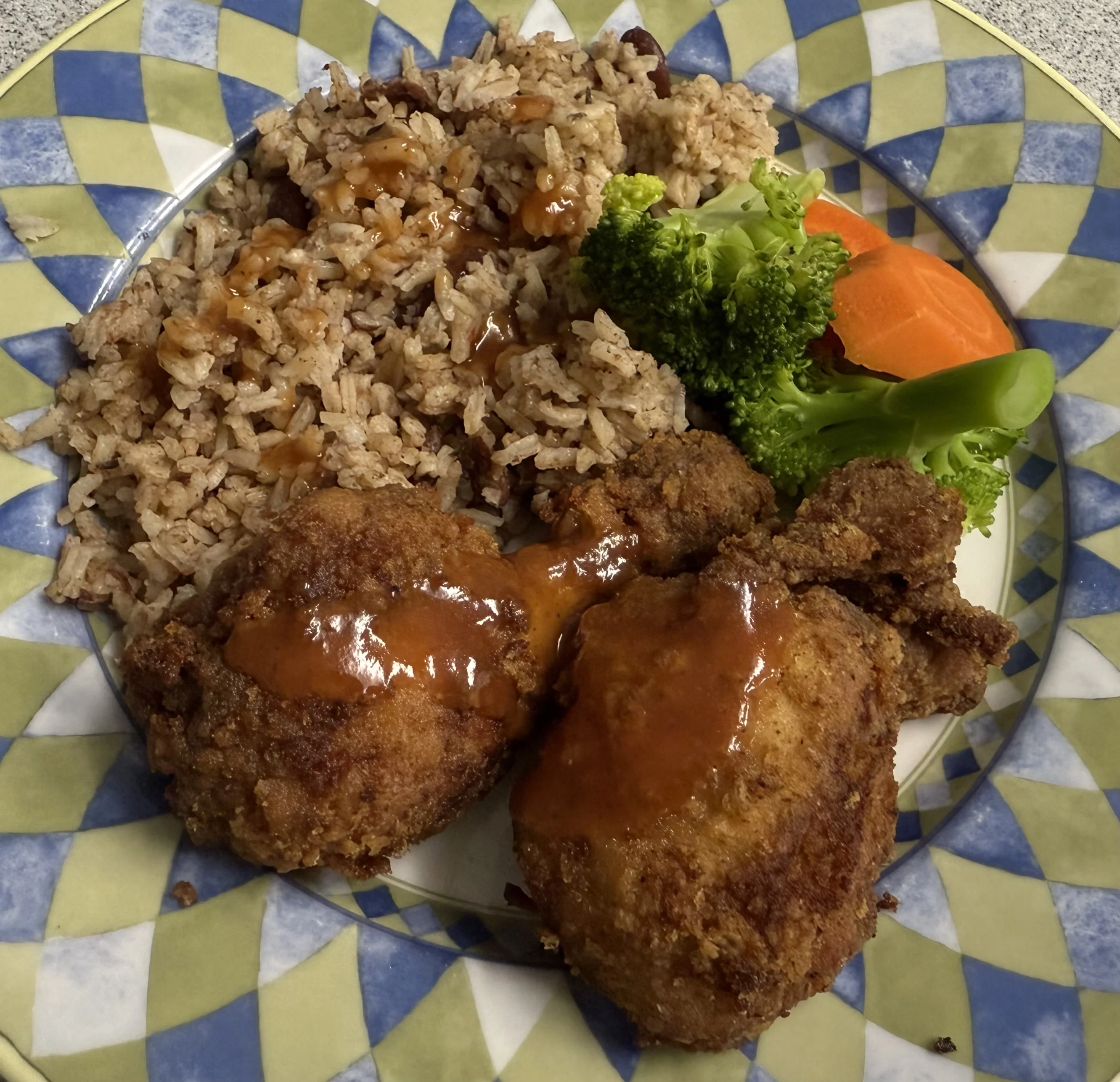 Rice and beans plated with fried chicken, broccoli and carrots